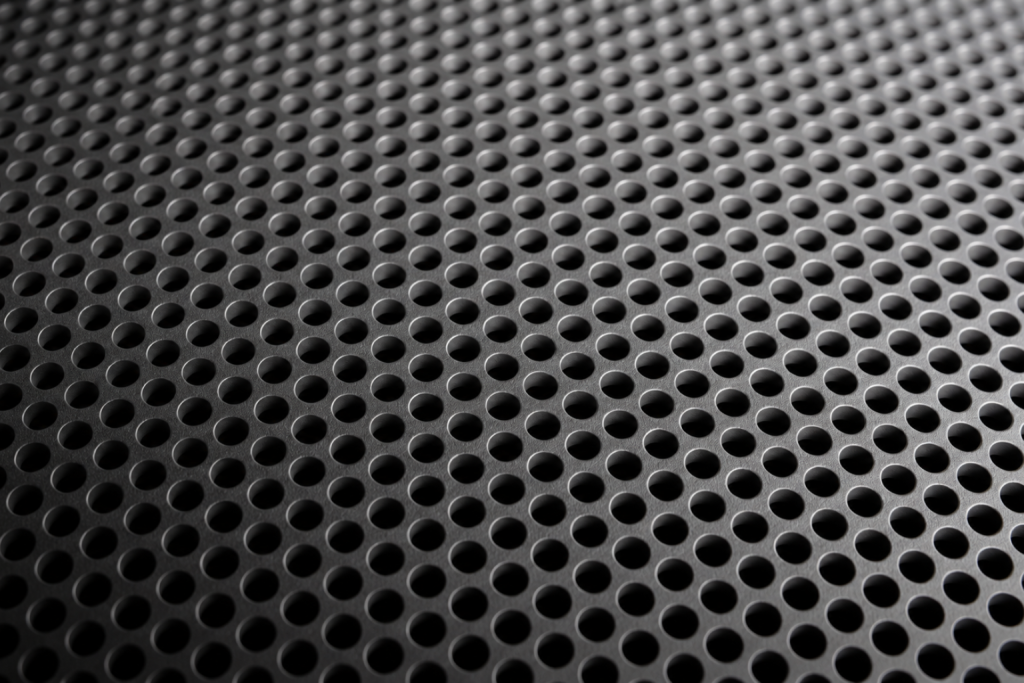 Pieza industrial gris con geometría mecanizada, ranuras profundas y secciones verticales de diferentes espesores, vista de cerca.